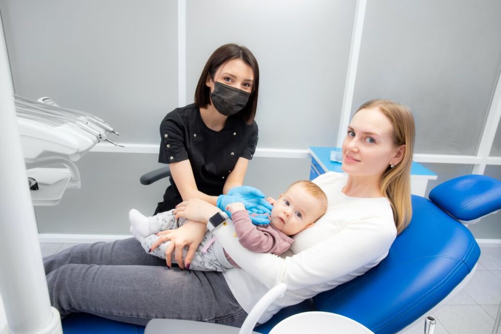 A woman sitting in a dental chair holding a baby